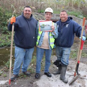 Shown from left to right: Sewer and Drain Supervisor Frank D’Amelio, Tuscano Avenue resident Rocco Falzone and Sewer and Drain Foreman Joseph Belcastro inside the Tuscano Avenue storm drain early on Sunday. Falzone is shown holding a flooding photo from 2024.