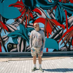 French muralist Julien Colombier is shown in front of his 2,700-square-foot mural at Amaya, the first residential building at Suffolk Downs. (Courtesy photo)