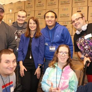 Kneeling, shown from left to right, are: Triangle, Inc. participants Kyle Colbert and Elizabeth Mathis. Back row, shown from left to right, are: Triangle Inc. Community Coordinator Jack Morris, Michael Barbera, Triangle Inc. CEO Rachel Kaprielian, Christopher Duong, and Robert Boyd stuffed frozen chicken into bags for elderly and disabled Malden and Everett seniors.