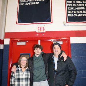 GREAT COMPANY: Parents Danielle and William Day with their son, Ethan stand under the banner marking Ethan’s 1,000 points scored playing for the Pats.