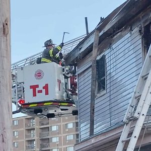 A firefighter is shown tearing at debris hanging from the Devens Street home on Tuesday.
