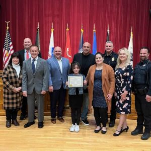 A COMMENDATION: Camila Giron Guardado (front row, left), 9, displays the citation she received from the Board of Selectmen for “heroic action during a time of emergency.” Joining the young hero, pictured from left to right: Front row: her mother, Celina Guardado de Giron; Board of Selectmen Chair Debra Panetta; and Saugus Police Officer Tom DiPietro; second row: Selectman Corinne Riley, Selectman Michael Serino, Board of Selectmen Vice Chair Jeffrey Cicolini, Selectman Anthony Cogliano and Saugus Police Chief Michael Ricciardelli; back row: Town Manager Scott C. Crabtree. (Courtesy photo to The Saugus Advocate)