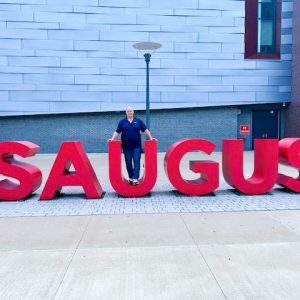 APPRECIATING TOWN SUPPORT: Guy Moley, the driving force behind Mom’s Cancer Fighting Angels Car Shows, stands near the entrance of the Saugus Middle-High School. Moley recently expressed gratitude to the town that he was able host a car show fundraiser in the school parking lot. (Courtesy Photo of Joanie Allbee)