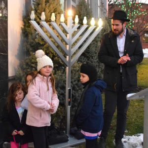 Children assist Rabbi Sruli Baron in lighting the menorah.