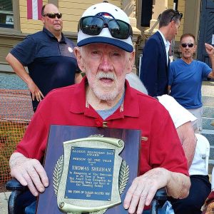 FOUNDERS DAY 2022: Saugus historian and longtime book author and writer Tom Sheehan sat in front of Town Hall last year holding the plaque he received for being named “Person of The Year.” (Saugus Advocate file photo by Mark E. Vogler)
