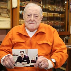 ABC Cigar co-owner Dan Moore holds a photo of himself at the age of 32, as a member of the U.S. Treasury Dept., when he was assigned to protect First Lady Jackie Kennedy following the assassination of President John F. Kennedy. (Advocate photo by Tara Vocino)
