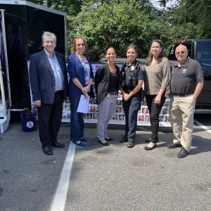 In front of a banner displaying pictures of the deceased are Drug Awareness Committee members and Saugus police, pictured from left to right: Chairperson Ron Visconti, Annamaria Filkins, Detective Stacy Forni, Police Officer Jenna Loverme, Jeannine Breau and Bill Pothier.