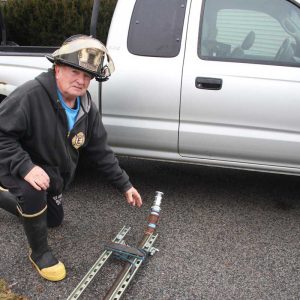 Retired Everett Fire Capt. Gerry O’Hearn kneels by the hose that goes underneath the engine.