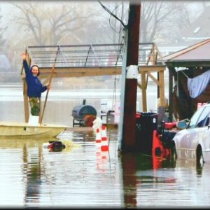 ON THE WATER’S EDGE: A Ballard Street resident waves to the photographer as he uses his boat to get around his flooded property. (Courtesy Photo to The Saugus Advocate by Charlie Zapolski)