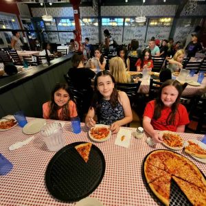 PASTA DINNER: Pictured from left to right: Alanah Sullivan, Naomi Tarantino and Amelia Clark, with teammates behind them, enjoyed some camaraderie and pizza last Friday (July 7) at Prince Pizzeria. They met the next day for a meet at Serino Stadium. They are part of a group of young athletes from Chris Tarantino’s summer track camp who will be headed down to Cranston, Rhode Island, tomorrow (Saturday, July 15) for a region-wide competition. (Courtesy photo to The Saugus Advocate by Chris Tarantino)