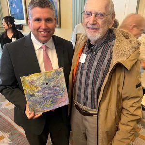 Resident Fred Kolb of Golda Meir House presents a painting to State Senator Sal DiDomenico.
