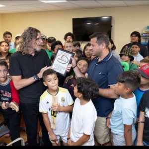 Ernie Boch, Jr. (left) is shown presenting a plaque to Michael Lenson, program manager for MGH Revere Youth Zone, marking the occasion after the philanthropist donated musical equipment through his music foundation, Music Drives Us.