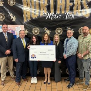 THIRD-PLACE WINNER: Massachusetts Treasurer and Receiver General Deborah B. Goldberg (at center in blue) presented a $100 check to Northeast Metro Tech senior Design and Visual Communications student Kacey Kellum. From left to right: Principal Richard Barden, MSBA CEO James MacDonald, Kellum, Goldberg, Assistant Superintendent Tracey O’Brien, Assistant Principal Jack O’Brien and Design and Visual Communications Instructor Brian Peluso. (Photo Courtesy Northeast Metro Tech)