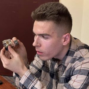 Perfect Pastime 617 Founder/CEO Rick Keller is shown examining a perfume bottle at the Parlin Memorial Library in March 2025. (Courtesy photo)