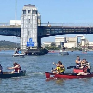 Competitors row down the Pines River with the WIN Waste Innovations facility in the background.