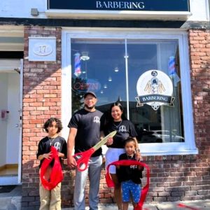 A NEW BARBER SHOP: Edison and Brenda Breton, with their two children, Daniel and Sofia, stand at the entrance of Clean & Dapper, after a ribbon-cutting to celebrate their business opening at 17 Essex St. this week. (Courtesy photo to The Saugus Advocate).