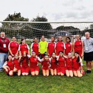 Saugus Impact, a G8 girls soccer team, relaxes after a recent win over Lawrence. Pictured from left to right: first row: Keira Kinder, Isobel Penza, Emma Leo, Amani Guenanou, Sophia Coelho, Lucia Giron, Juliana Valentine, Brooke Foley, Vittoria Valentine; second row: Coach Mike Hashem, Alexa DeModena, Riley Moses, Victoria Tum, Kaitlyn Hashem, Alannah Duong, Georgia Condakes, Selena Garcia, Ava Foley and Coach Mike Bluette. Missing from photo: Julia Loberg. (Courtesy photo to The Saugus Advocate)