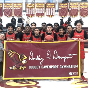 CRIMSON TIDE PRIDE: Coach Gerard Boyce, third, right, and his Everett boys basketball team proudly pose with the Dudley Davenport Tournament banner after beating Sharon, the host team, in the championship game on Tuesday, Feb. 18. The win clinches a berth in the Division 1 state tournament for the Crimson Tide. (Courtesy photo)