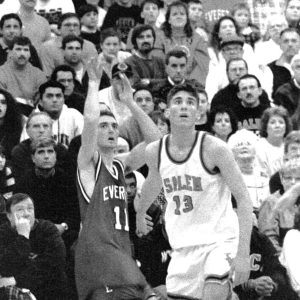 BRADLEY FOR THREE: “E” Club guest speaker Pat Bradley led Crimson Tide varsity basketball team to the Eastern Mass. final (’94) and Eastern Mass. North final (’95), and became the school’s all-time leading scorer, among other accolades. In this photo, Bradley and a Salem opponent watch one of Pat’s three-point shots sail into the basket at a very humid and packed Northeast Regional Vocational High School fieldhouse in Wakefield in 1994.  (Advocate file photo)